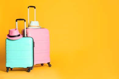 Photo of Travel suitcases with hats on yellow background, space for text. Summer vacation