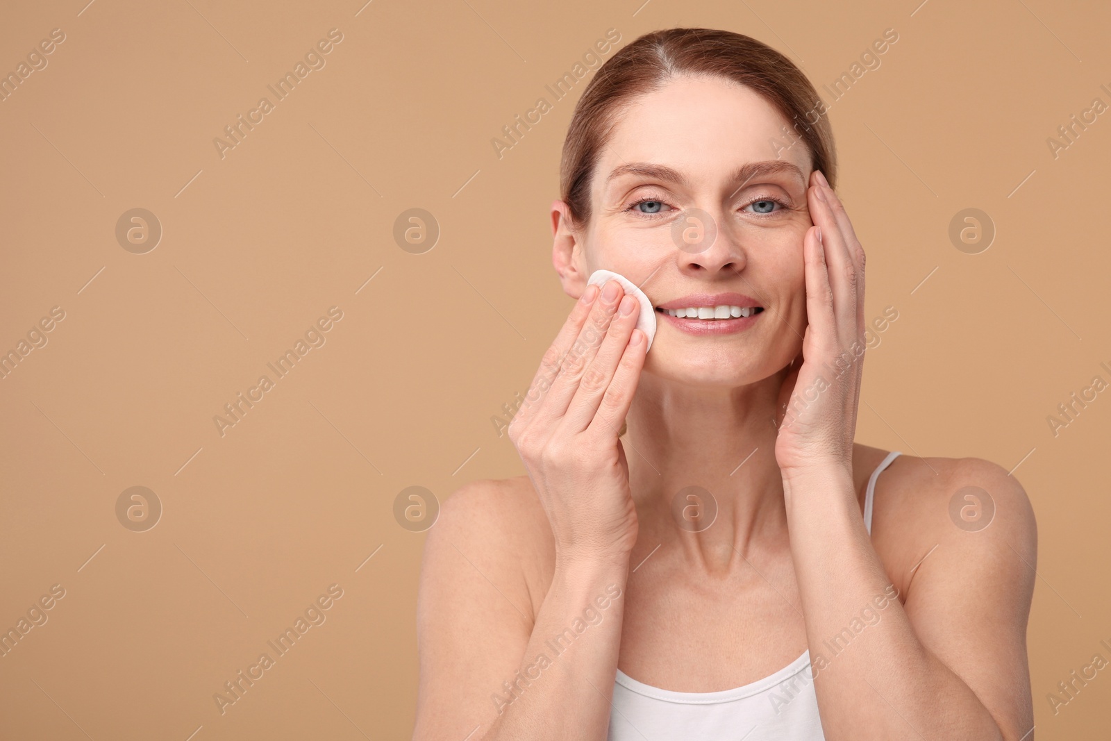 Photo of Beautiful woman removing makeup with cotton pad on beige background, space for text