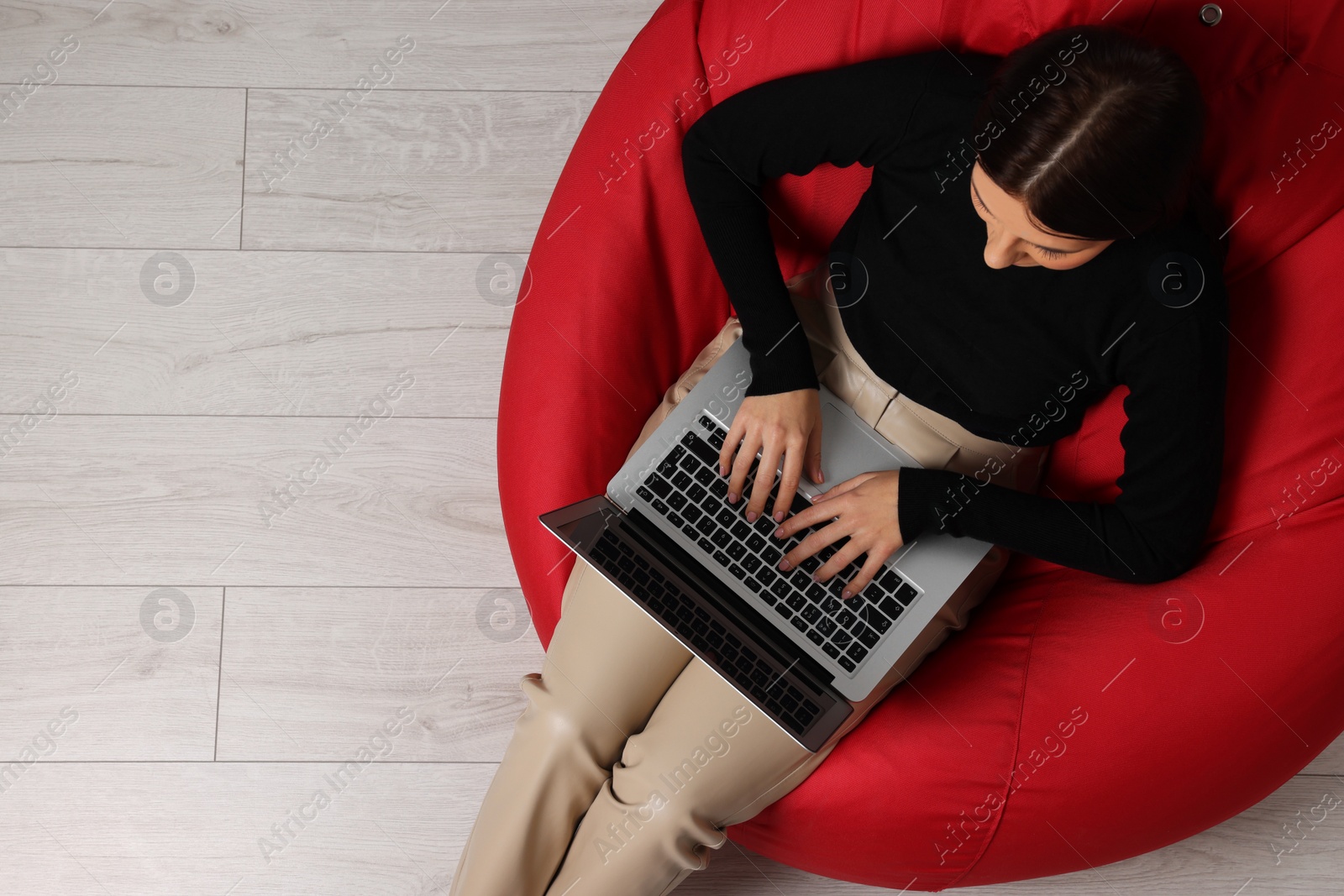 Photo of Woman working with laptop in beanbag chair, top view. Space for text