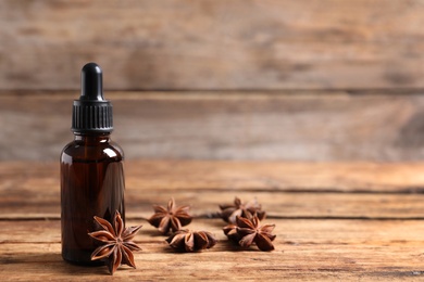 Bottle of essential oil and anise on wooden table. Space for text