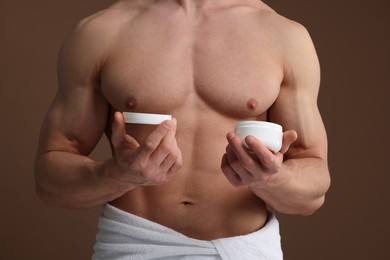 Photo of Handsome man holding jar with moisturizing cream on brown background, closeup