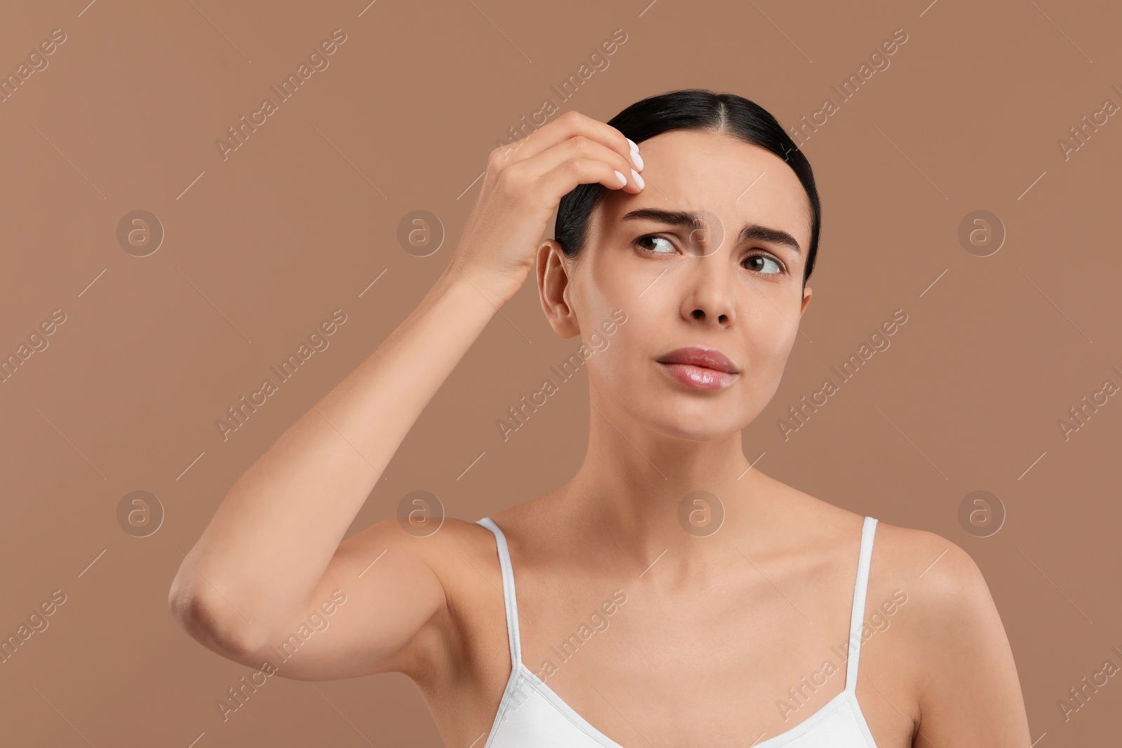 Photo of Woman with dry skin checking her face on beige background