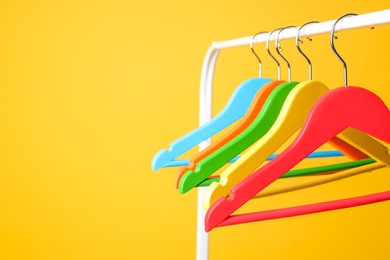 Photo of Bright clothes hangers on metal rack against yellow background, closeup. Space for text