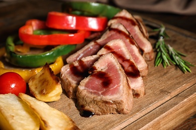 Photo of Cut roasted meat served with sauce and garnish on wooden board, closeup