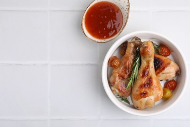 Photo of Marinade, roasted chicken drumsticks, rosemary and tomatoes on white tiled table, flat lay. Space for text