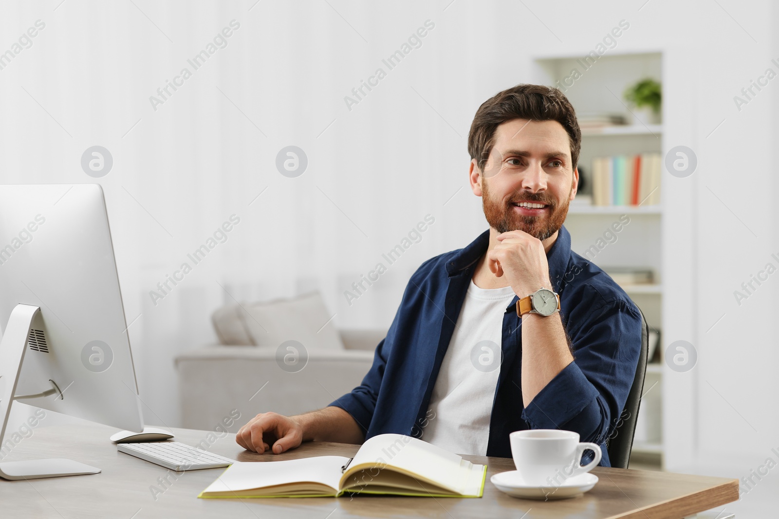 Photo of Home workplace. Happy man at wooden desk with computer in room