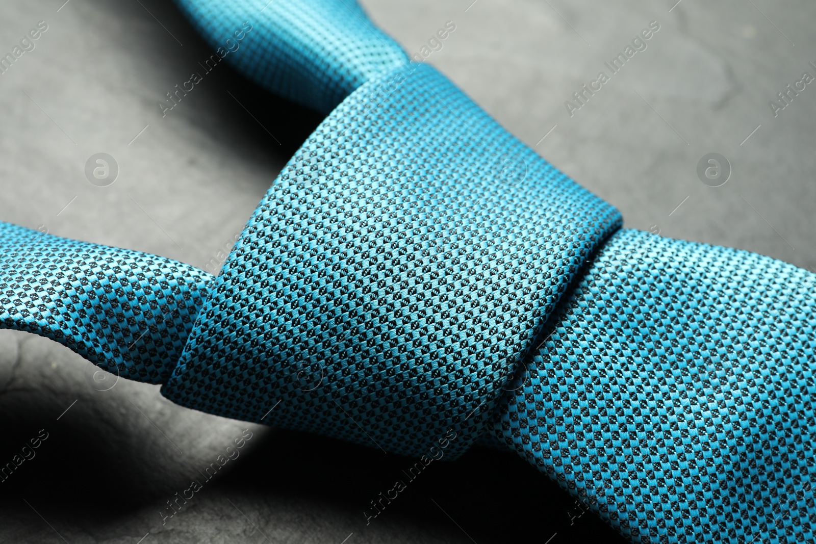 Photo of One light blue necktie on grey textured table, closeup