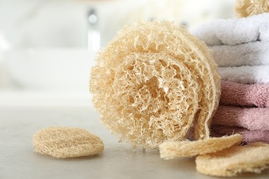 Photo of Natural loofah sponges and towels on table in bathroom, closeup