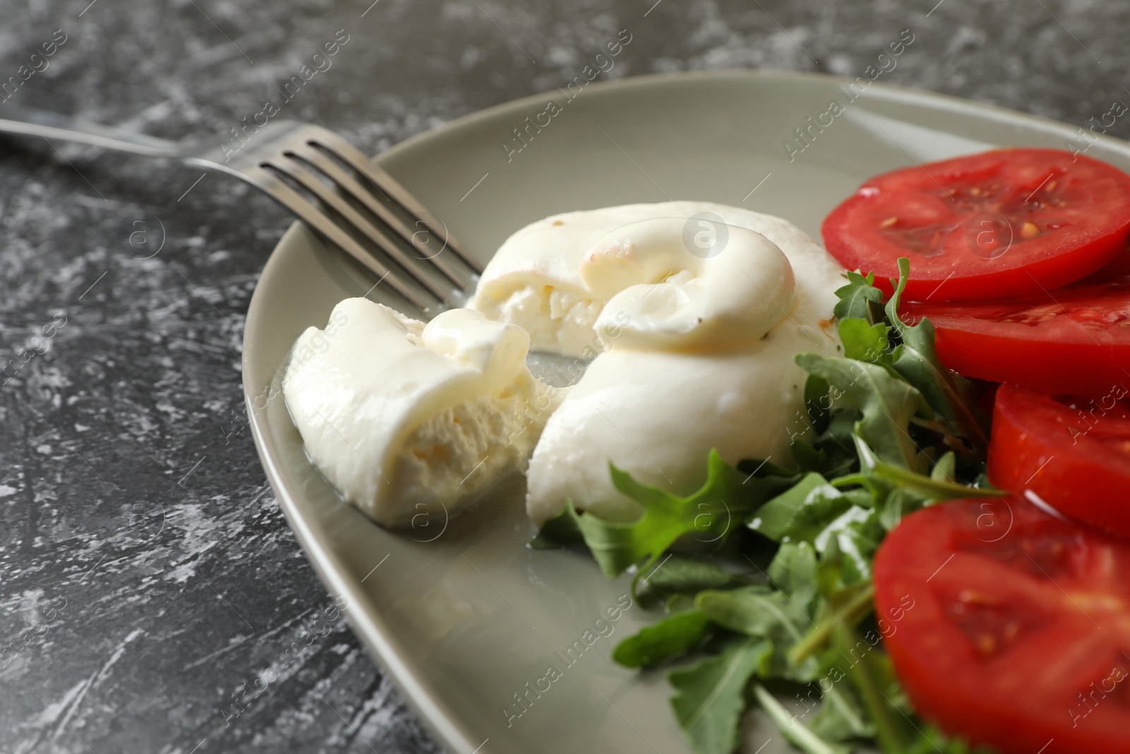 Photo of Delicious burrata cheese with tomatoes, arugula and fork on grey table, closeup