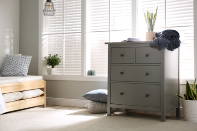 Grey chest of drawers near window in stylish bedroom interior
