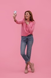 Beautiful woman taking selfie on pink background