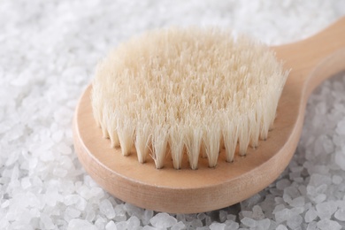 Photo of White sea salt for spa scrubbing procedure and brush, closeup