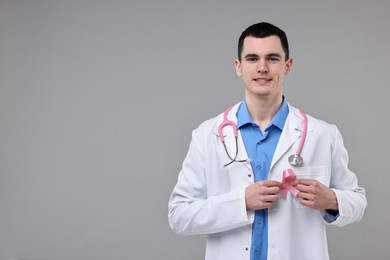 Portrait of smiling mammologist with pink ribbon and stethoscope on grey background. Space for text