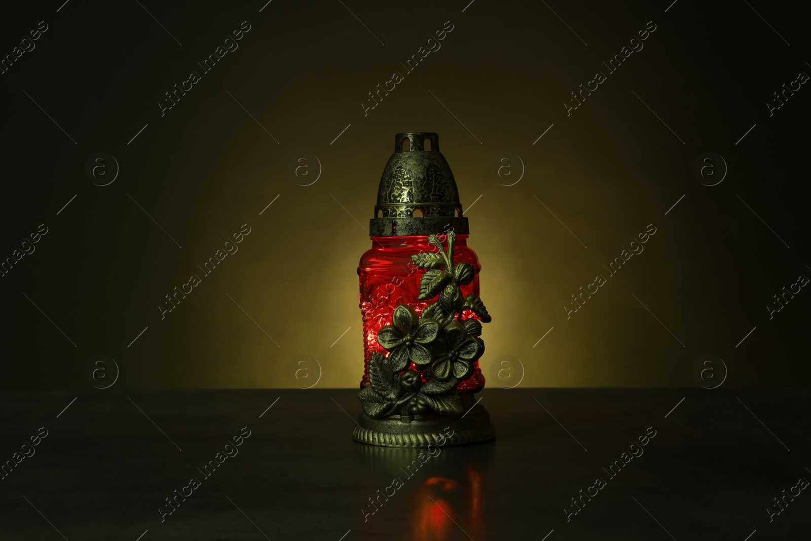 Photo of Beautiful glowing red grave light on table in darkness. Symbol of remembrance