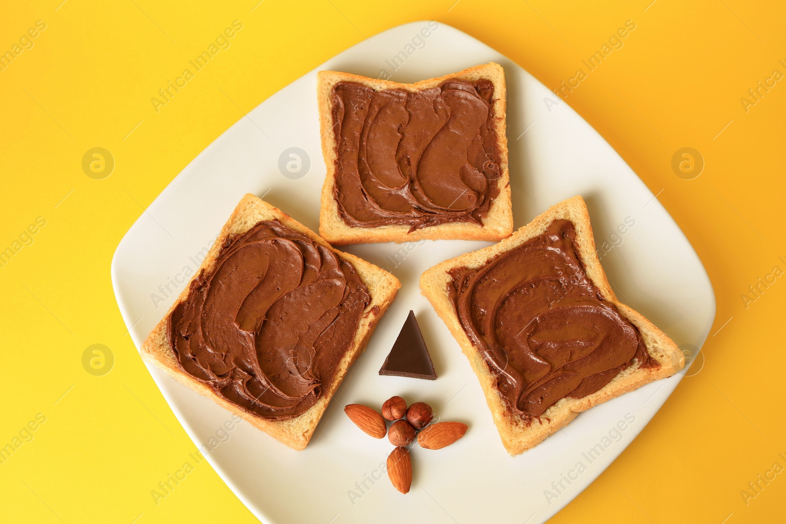 Photo of Tasty toasts with chocolate paste and nuts on yellow background, above view