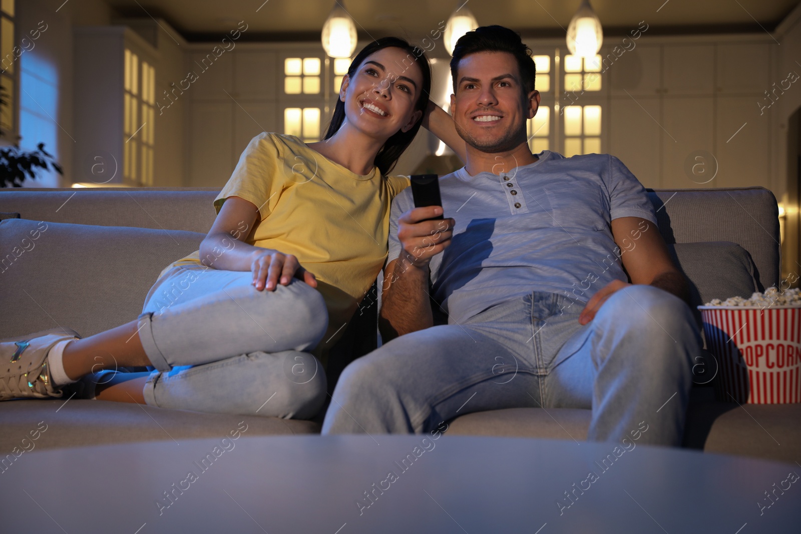 Photo of Couple watching movie with popcorn on sofa at night