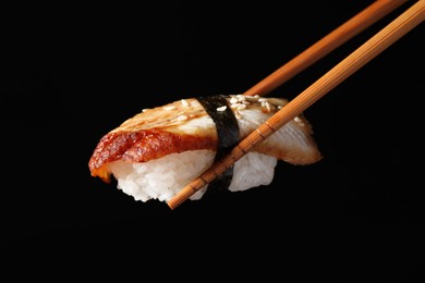 Photo of Chopsticks with delicious nigiri sushi on black background, closeup