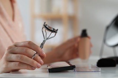 Woman with eyelash curler at dressing table indoors, closeup. Space for text