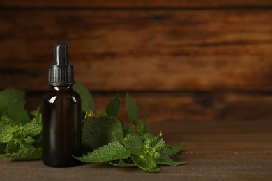 Photo of Glass bottle of nettle oil with dropper and leaves on wooden table, space for text