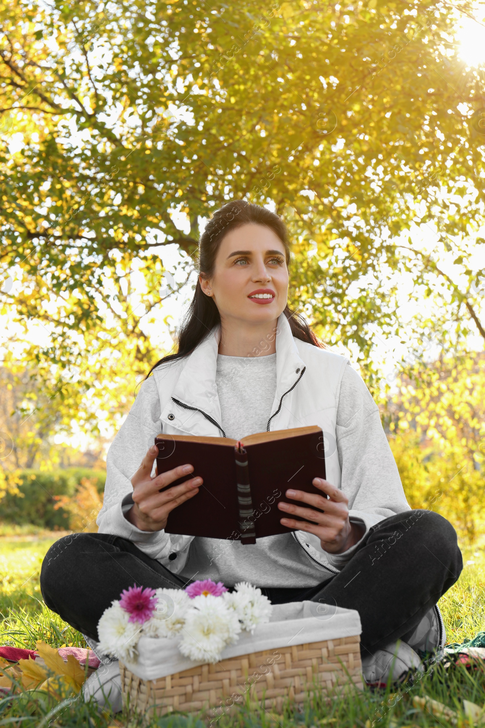 Photo of Happy woman reading book in park on autumn day