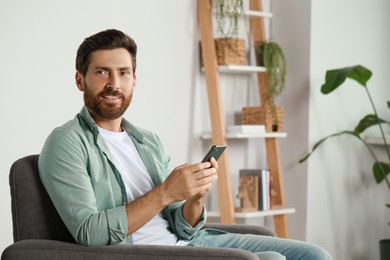 Handsome man with smartphone at home, space for text
