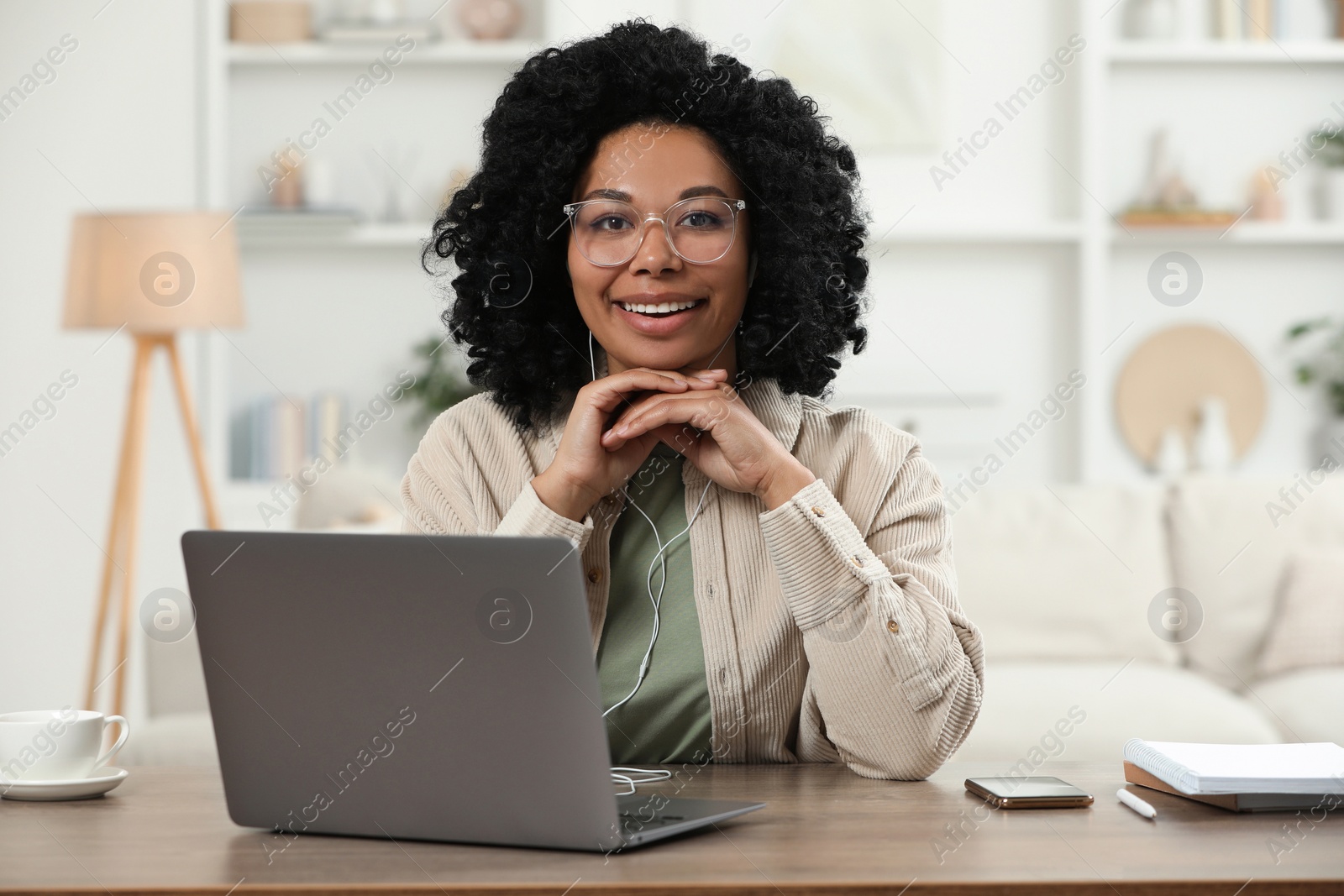 Photo of Happy young woman with laptop at wooden desk indoors