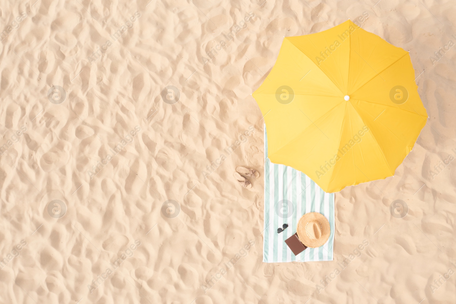 Image of Beach umbrella near towel and other vacationist's stuff on sand, aerial view. Space for text