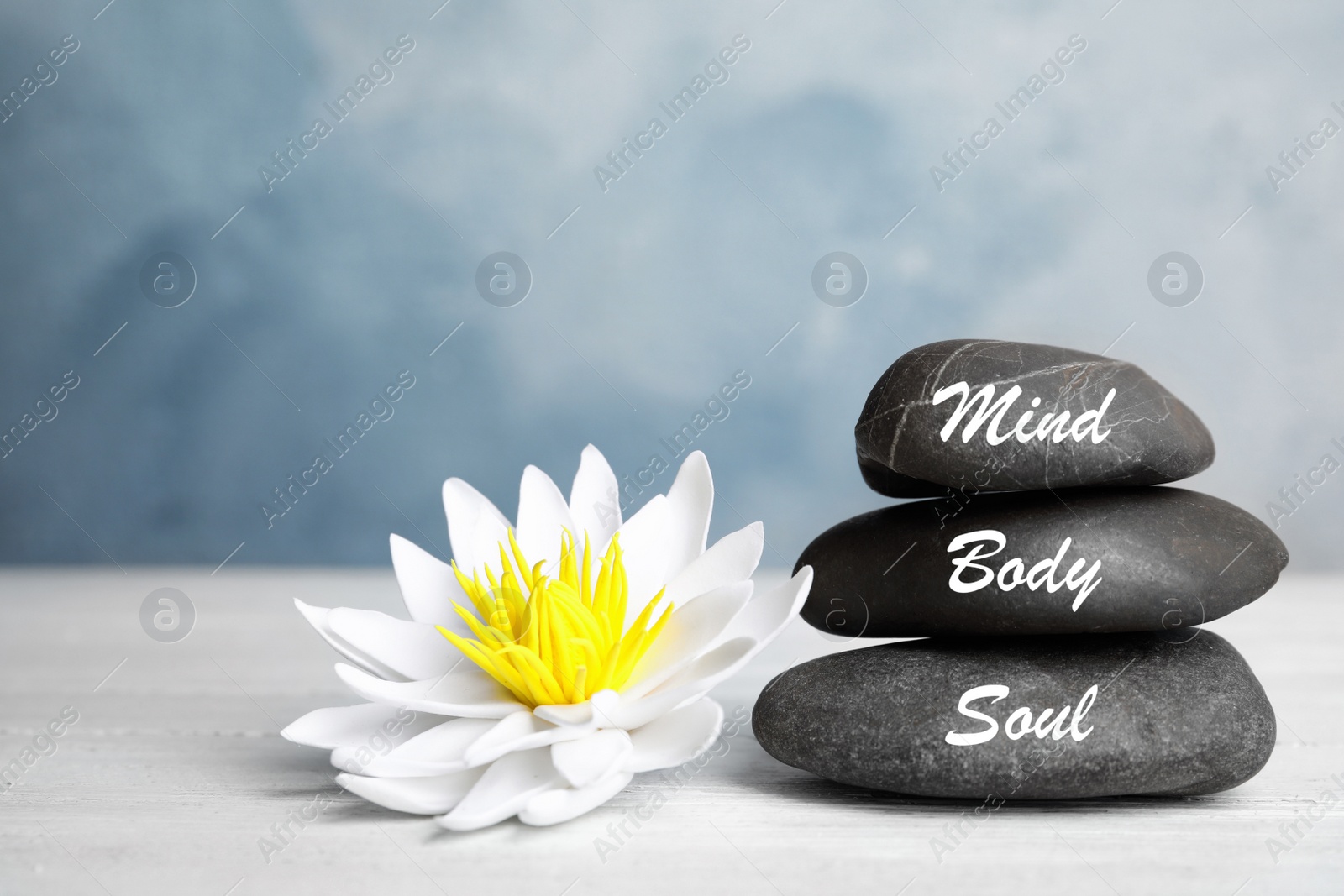 Photo of Stones with words Mind, Body, Soul and lotus flower on white wooden table. Zen lifestyle