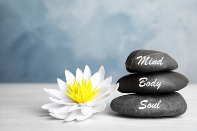 Photo of Stones with words Mind, Body, Soul and lotus flower on white wooden table. Zen lifestyle