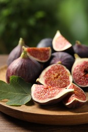 Photo of Whole and cut ripe figs with leaf on wooden table against blurred green background, closeup