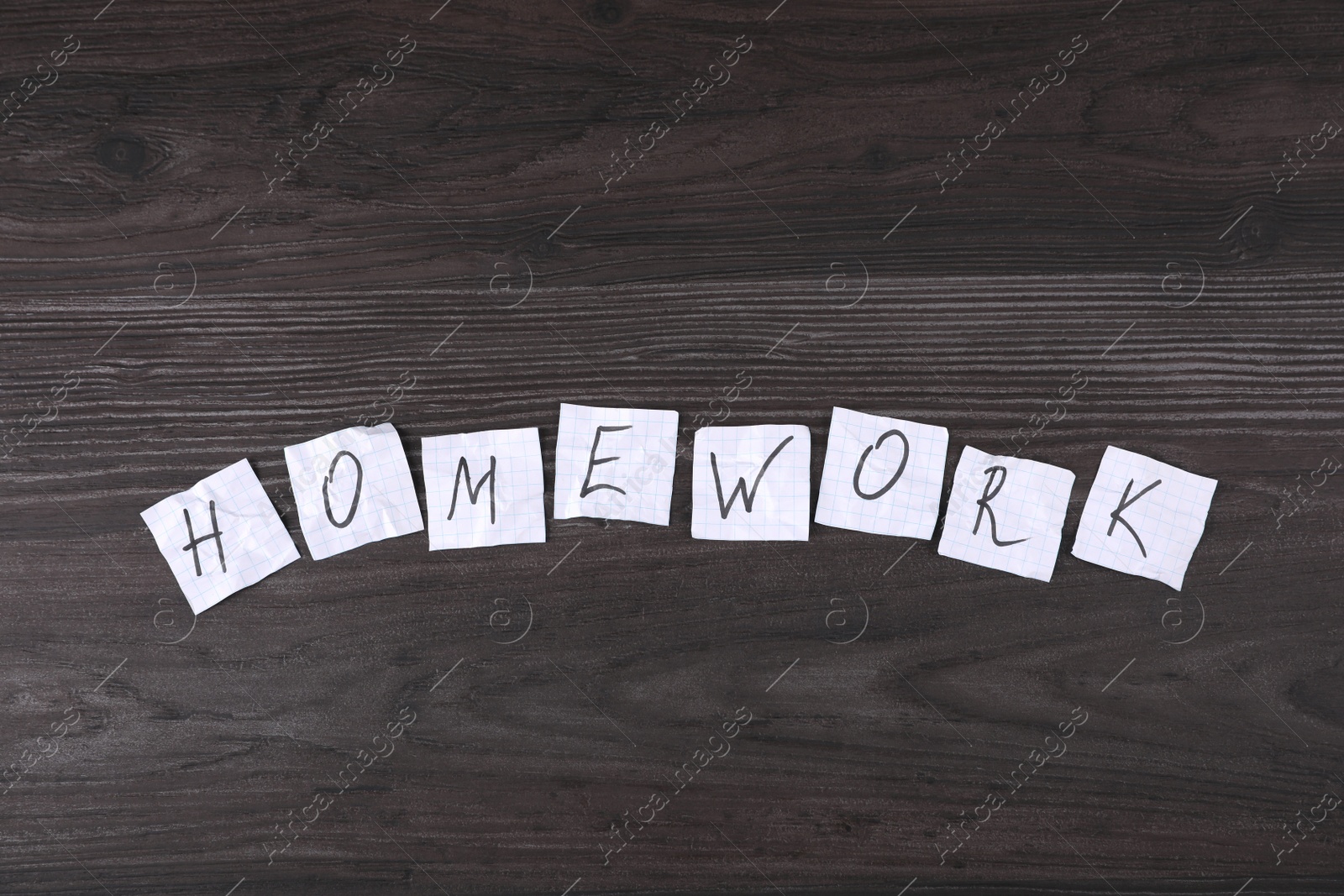 Photo of Word HOMEWORK made of pieces of paper on wooden table, flat lay