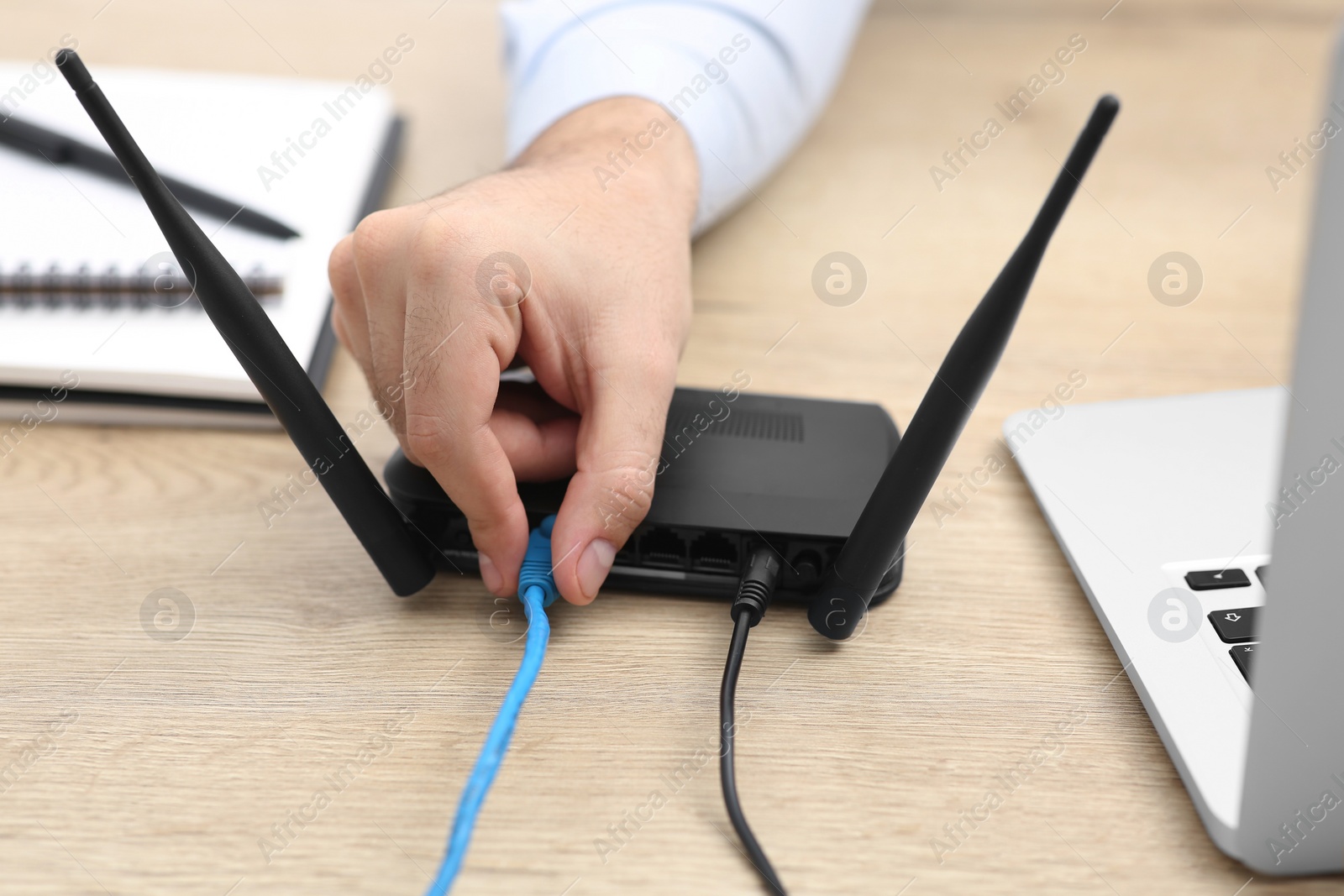 Photo of Man inserting cable into Wi-Fi router at wooden table indoors, closeup