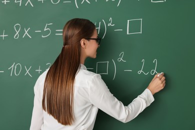 Photo of Young math’s teacher writing mathematical equations near chalkboard