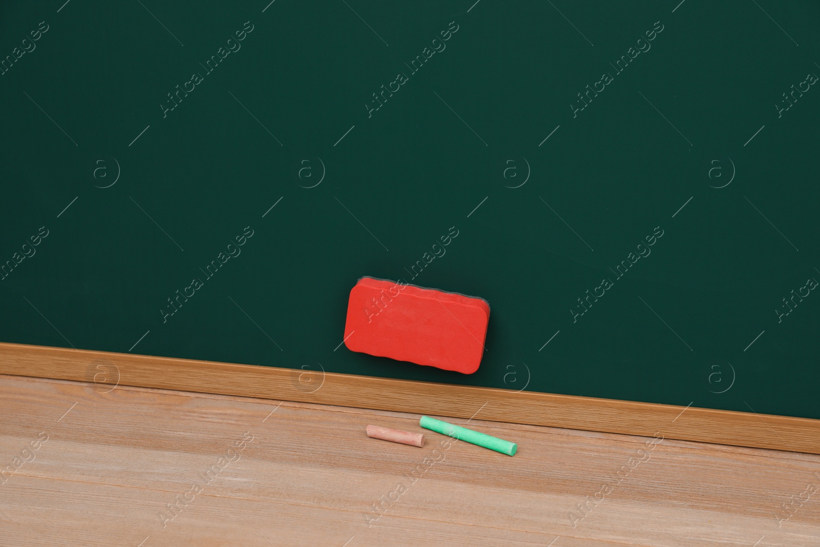 Photo of Colorful chalks on wooden table near green board with duster. Space for text