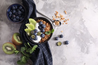 Photo of Tasty granola with yogurt, blueberries and kiwi in bowl on gray textured table, flat lay. Space for text