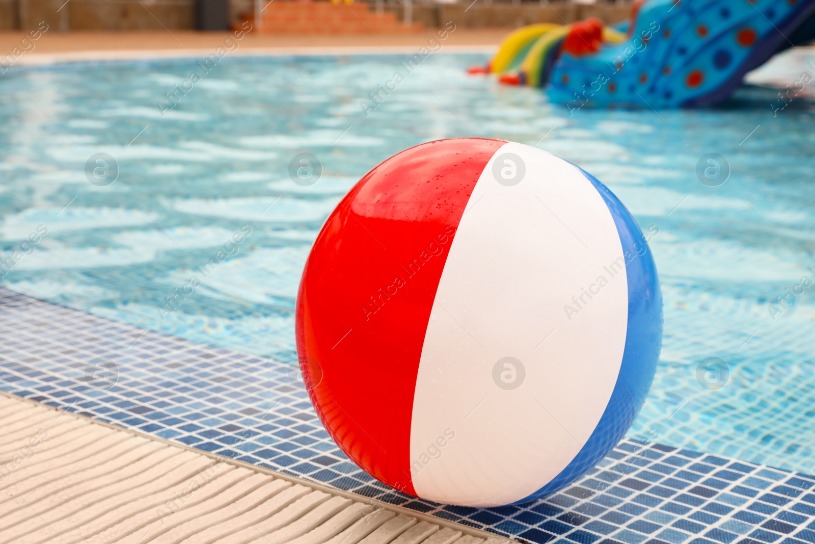 Photo of Inflatable colorful beach ball on edge of outdoor swimming pool, space for text