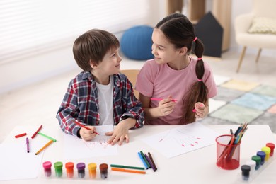 Happy brother and sister drawing at white table in room