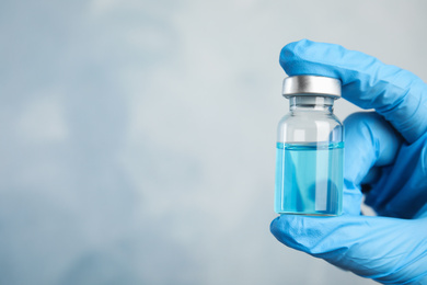 Doctor holding vial with medication on light blue background, closeup view and space for text. Vaccination and immunization