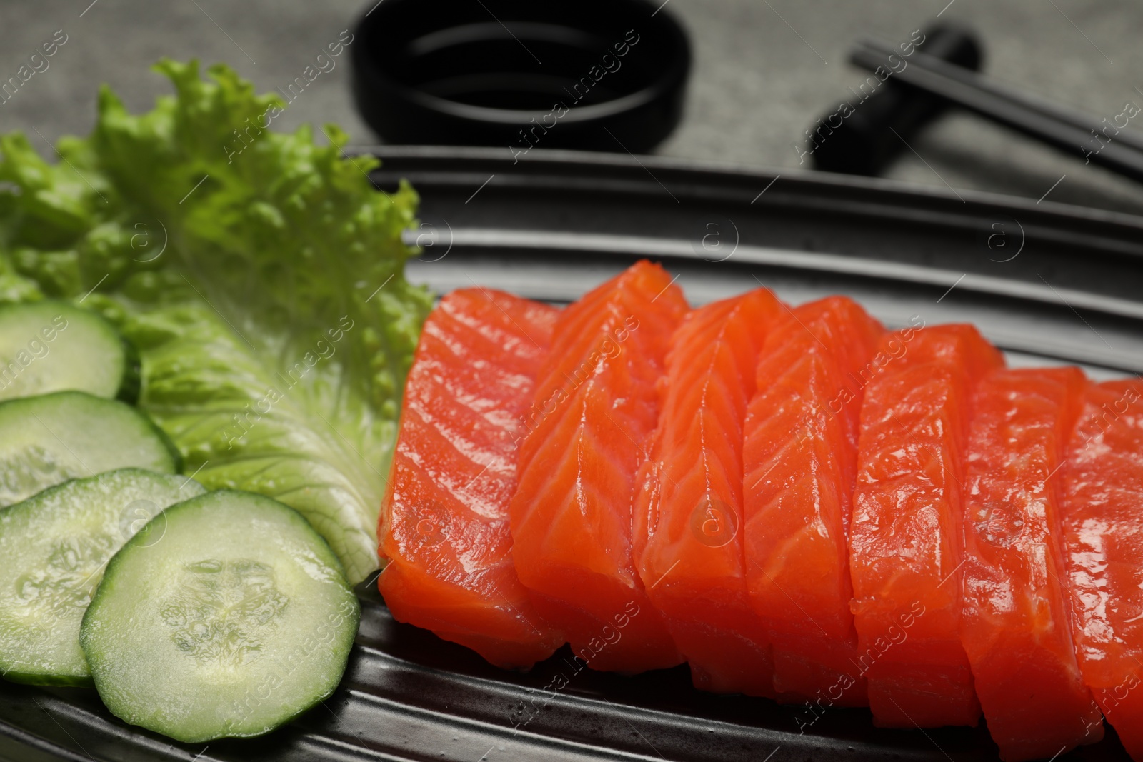 Photo of Tasty salmon slices, cucumber and lettuce on plate, closeup. Delicious sashimi dish