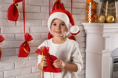 Photo of Cute little girl in Santa hat holding gift from Christmas advent calendar at home