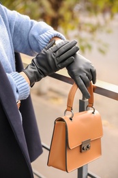 Young woman with stylish black leather gloves and bag outdoors, closeup