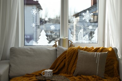 Cup of hot drink on sofa near window with beautiful drawing at home. Christmas decor