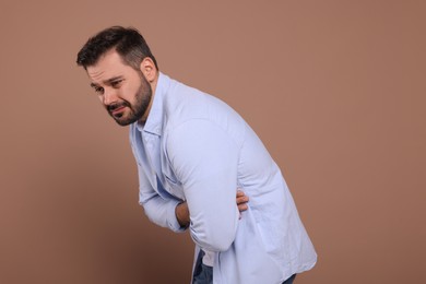 Photo of Unhappy man suffering from stomach pain on light brown background