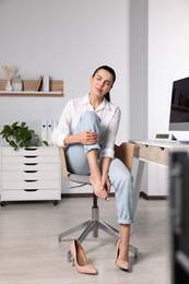 Photo of Young woman rubbing sore foot in office