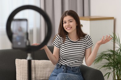 Photo of Smiling teenage blogger explaining something while streaming at home