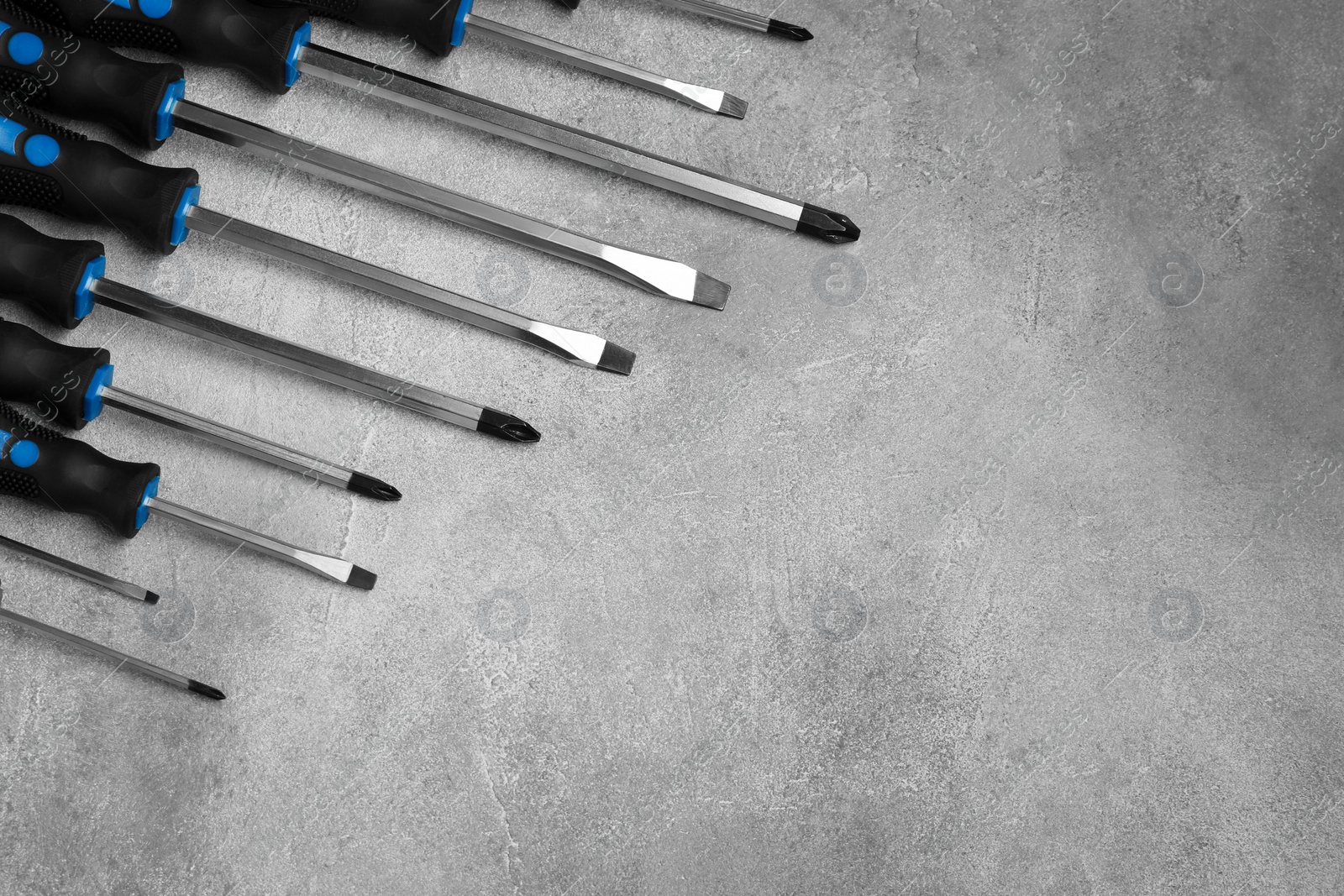 Photo of Set of screwdrivers on grey textured table, flat lay. Space for text