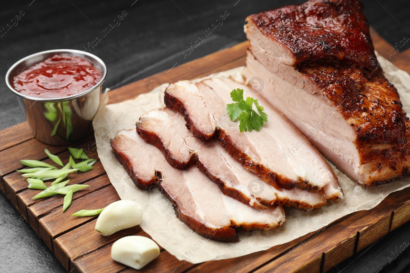 Photo of Pieces of baked pork belly served with sauce and parsley on black textured table