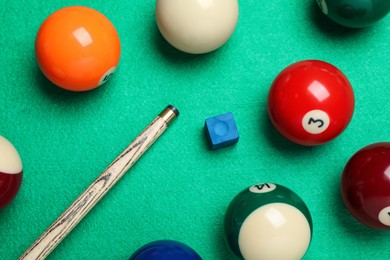 Set of billiard balls with cue and chalk on green table, flat lay