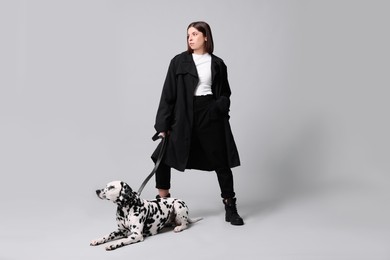 Beautiful young woman with her adorable Dalmatian dog on light grey background. Lovely pet