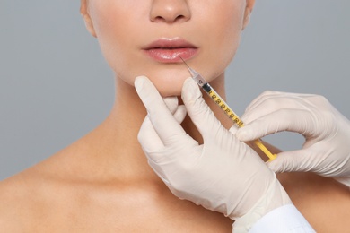 Young woman getting lips injection on grey background, closeup. Cosmetic surgery